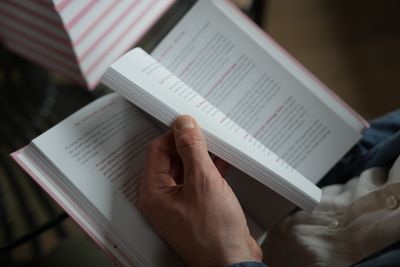 A hand flipping through the book, showing the pink-tinted page edges and red highlighted text