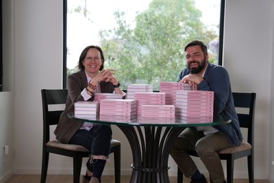 Sara and Mathias sitting together at a table stacked with copies of the finished book
