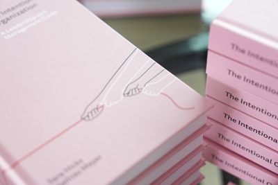 A close-up of the hardcover corner, showing the pink cover and the start of the cover illustration, with stacked copies blurred behind