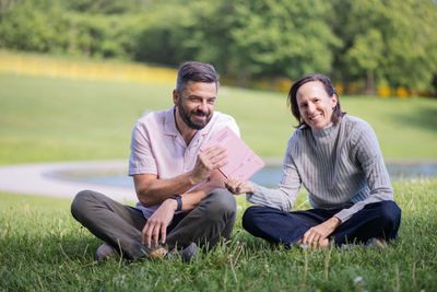 Sara and Mathias sitting outdoors together, both smiling, one holding a copy of the book