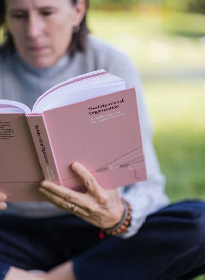 Sara reading The Intentional Organization outdoors, the book in soft focus against grass and trees